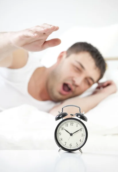 Спящий мужчина тянется за будильником — стоковое фото