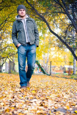 Genç adam sonbahar parkında yürüyor.