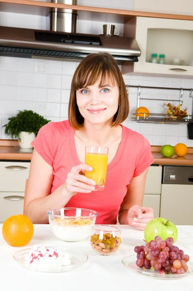 Mladá žena pít pomerančový džus s obilovin mušelínu doma — Stock fotografie