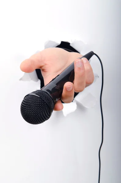 stock image Hand holding microphone through hole in paper