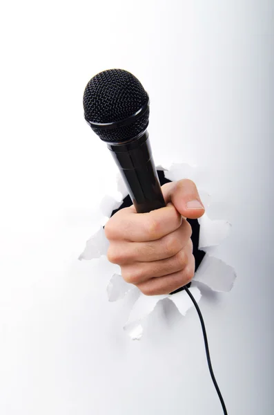Hand holding microphone through hole in paper — Stock Photo, Image