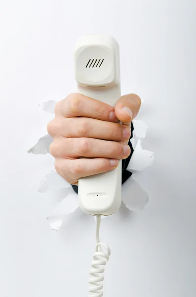 Hand som håller telefonen genom hål i papper — Stockfoto