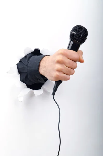 Hand holding microphone through hole in paper — Stock Photo, Image