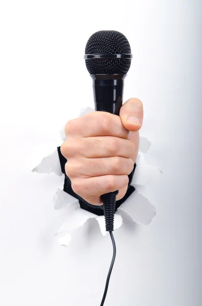 stock image Hand holding microphone through hole in paper