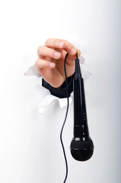 Mão segurando microfone através de furo em papel — Fotografia de Stock