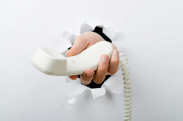 Mão segurando telefone através de furo no papel — Fotografia de Stock