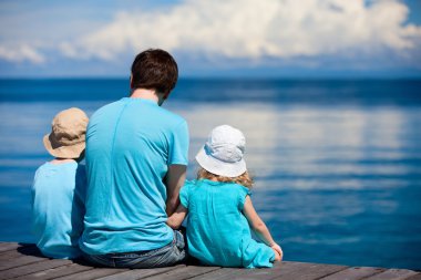 Father and kids sitting on wooden dock clipart
