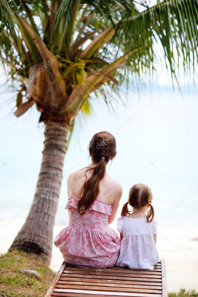 Mother and daughter sitting under palm