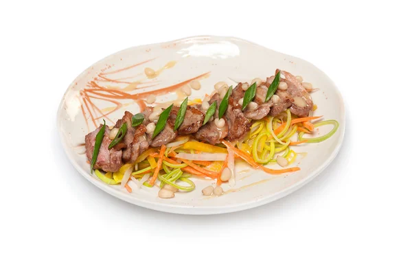 Gebakken rundvlees met saus, groenten, groene uien en pijnboompitten op een — Stockfoto
