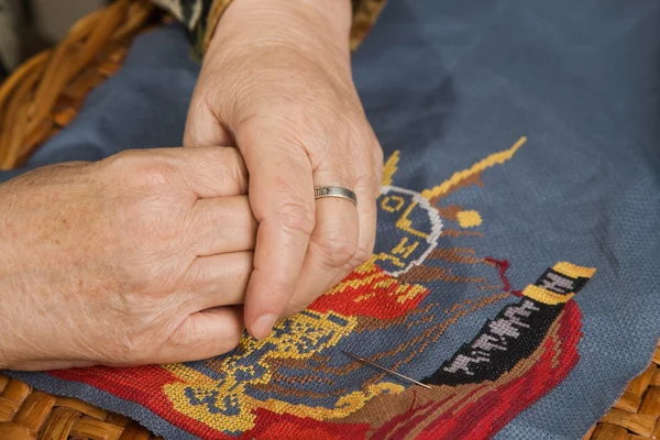 Old woman hand embroiders with a thread