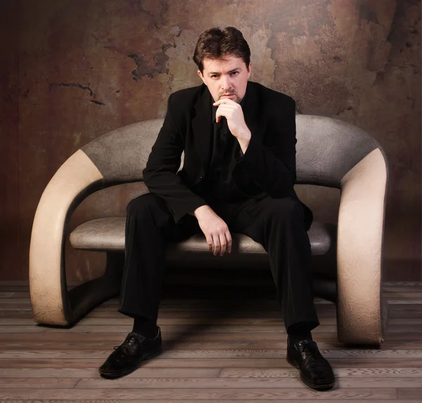 Человек в черном костюме сидит на диване — стоковое фото