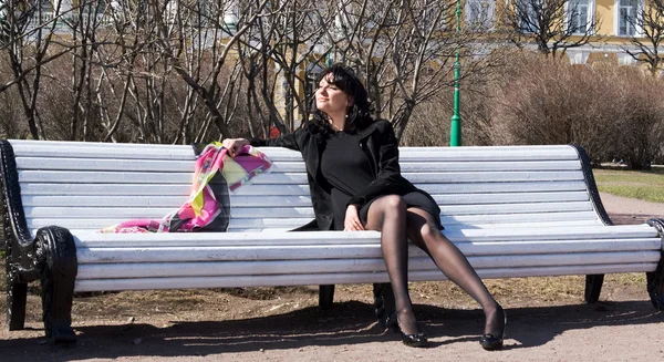 Schöne junge Frau sitzt auf einer Bank im Frühlingsgarten — Stockfoto