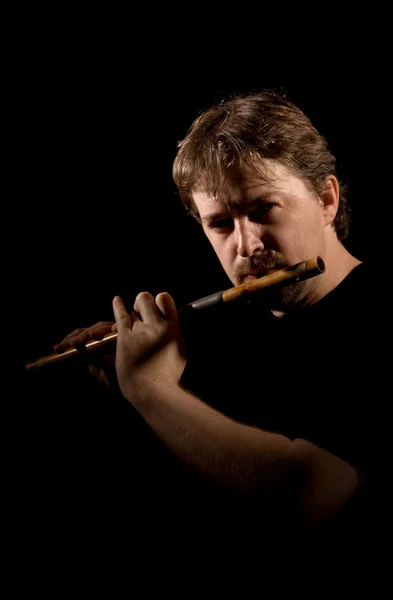 Человек в черном играет на флейте — стоковое фото