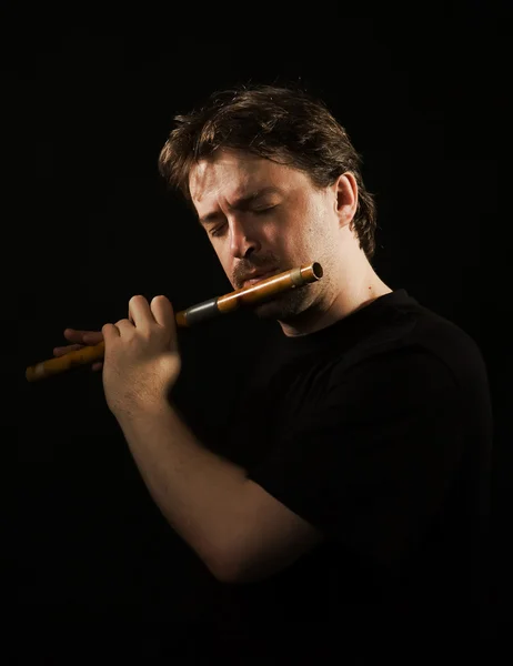 Muž v černém hraje na flétnu — Stock fotografie