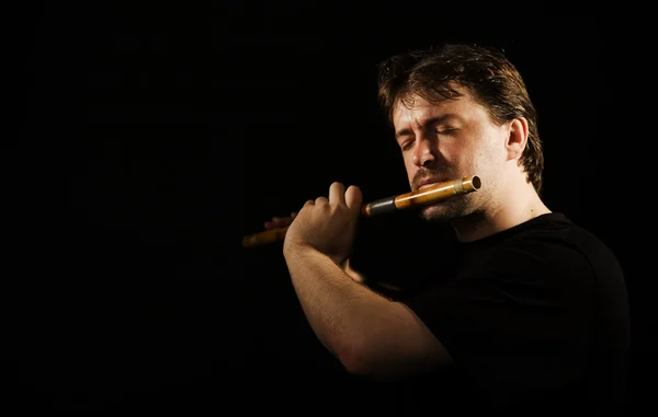 Man in black plays a flute — Stock Photo, Image