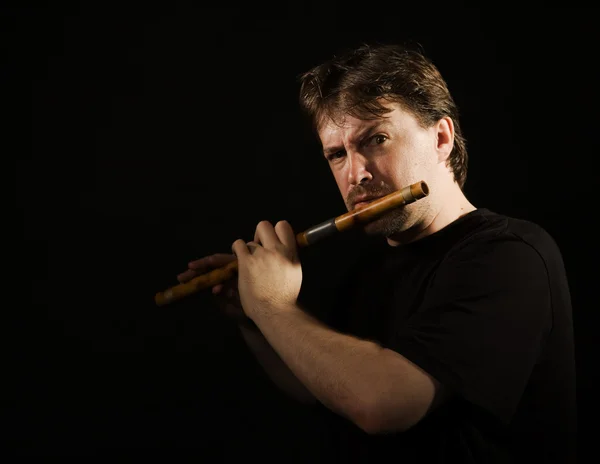 Человек в черном играет на флейте — стоковое фото