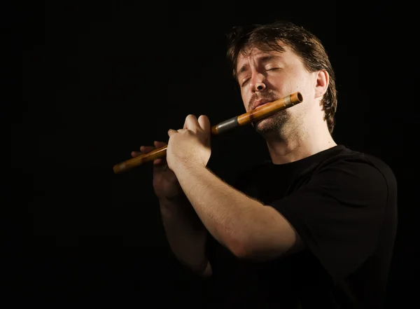 Muž v černém hraje na flétnu — Stock fotografie