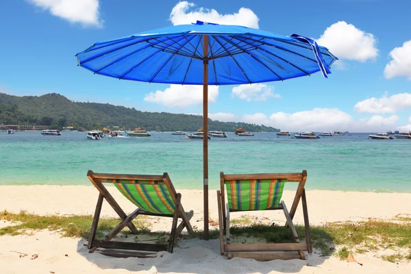 A blue beach umbrella and striped chaise lounges — Stock Photo, Image
