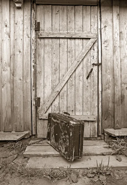 Old valise near wooden door, sepia — Stock Photo, Image