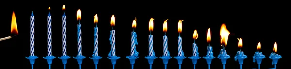 stock image Row of burning birthday candles and match stick on a black background