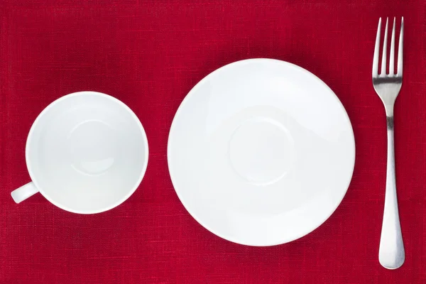 stock image Cup, plate and fork on red background