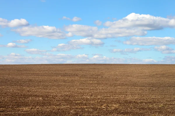 Campo arado e um céu azul nublado — Fotografia de Stock