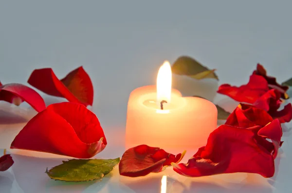 Una vela encendida en forma de corazón en pétalos de rosa —  Fotos de Stock