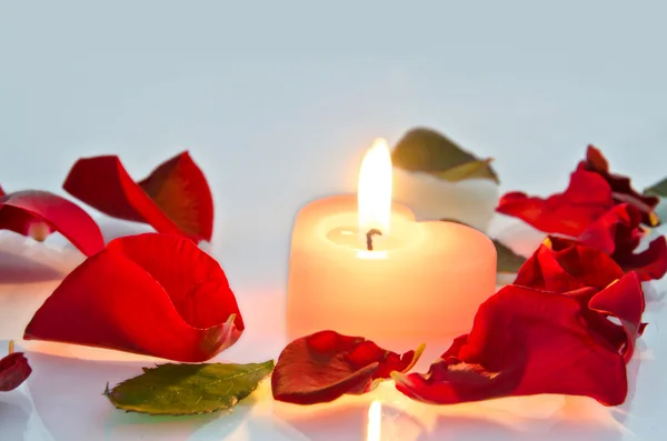 Una vela encendida en forma de corazón en pétalos de rosa —  Fotos de Stock