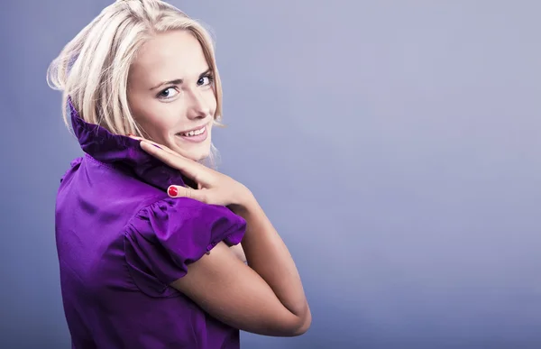 Modisches blondes Mädchen lächelt auf violettem Kleid. — Stockfoto