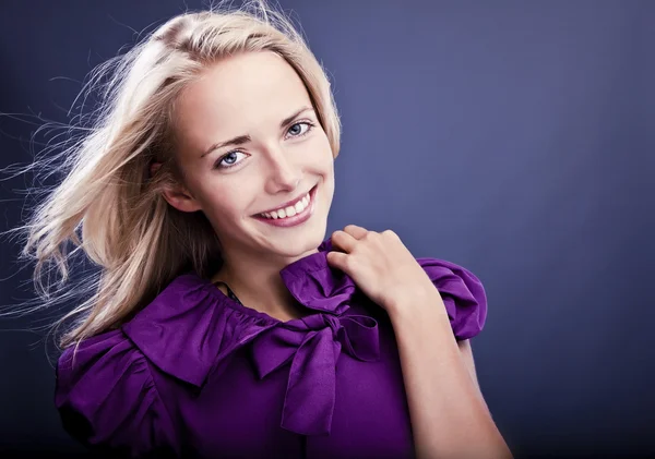 Modisches blondes Mädchen lächelt auf violettem Kleid. — Stockfoto