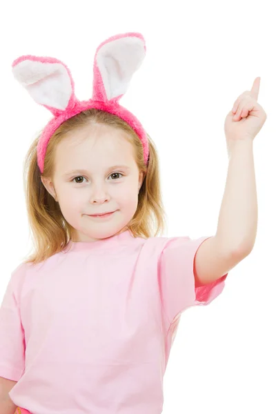 La petite fille aux oreilles roses pointe le lapin vers le haut sur fond blanc . — Photo