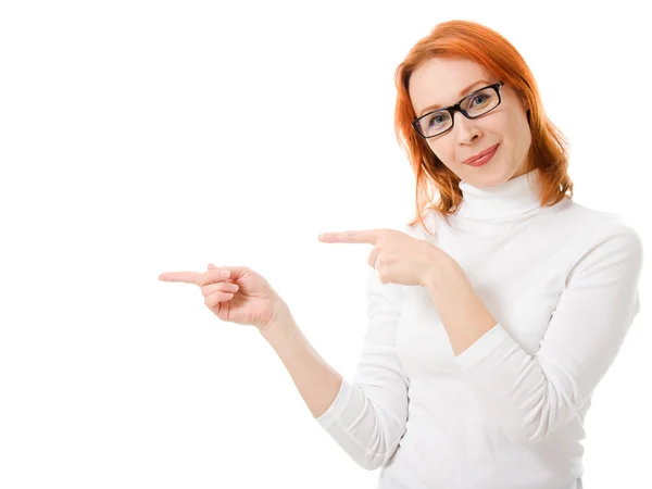 Uma menina bonita com o cabelo vermelho usando óculos aponta o dedo em um fundo branco . — Fotografia de Stock