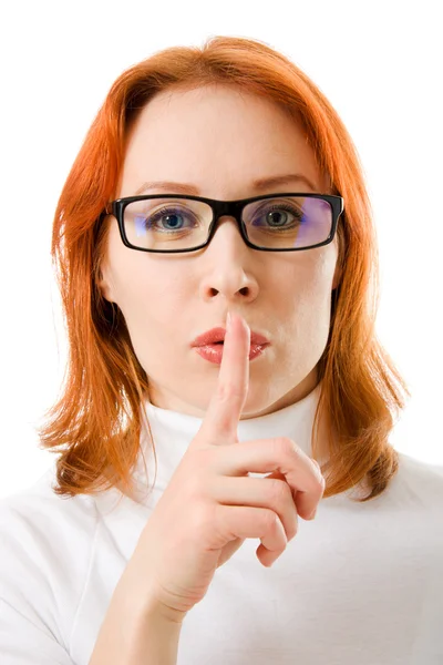 A beautiful girl with red hair wearing glasses silence points the finger at the white background. — Stock Photo, Image
