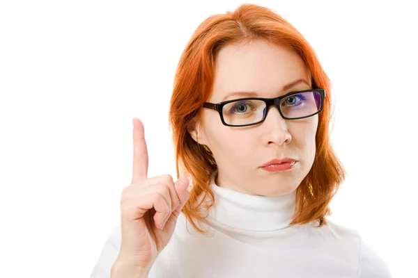 Uma menina bonita com o cabelo vermelho usando óculos aponta um dedo para cima em um fundo branco . — Fotografia de Stock