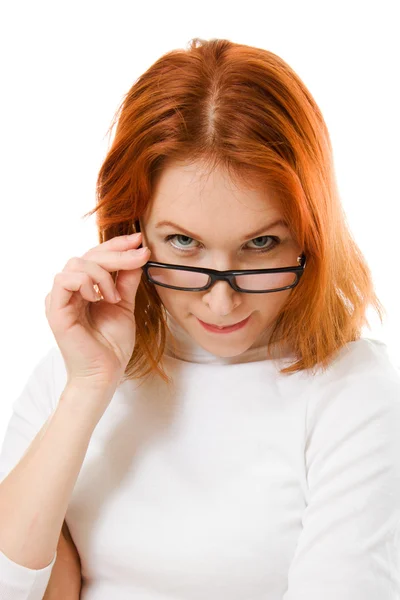 Een mooi meisje met rode haren kijkt uit glazen op een witte achtergrond. — Stockfoto