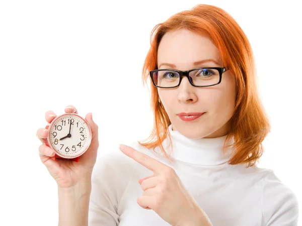 Ein schönes Mädchen mit roten Haaren und Brille zeigt mit dem Finger auf die Uhr auf weißem Hintergrund. — Stockfoto