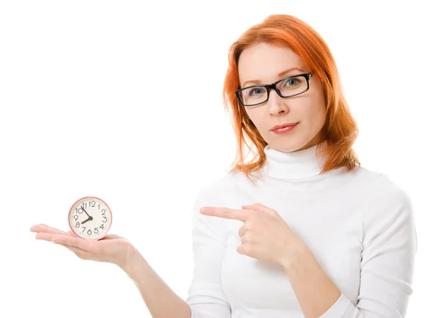Una bella ragazza con i capelli rossi con gli occhiali punta il dito contro l'orologio su uno sfondo bianco . — Foto Stock