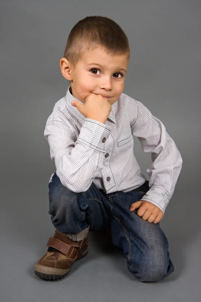 Chlapec sedí na šedém pozadí — Stock fotografie