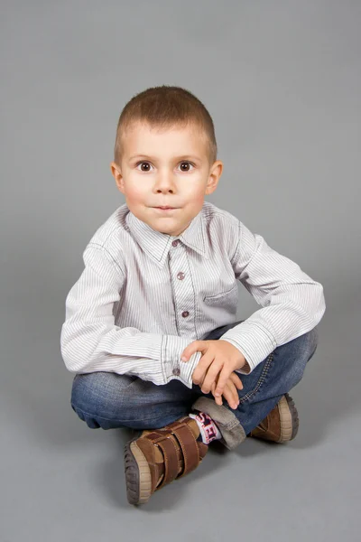 Хлопчик сидить на сірому фоні — стокове фото