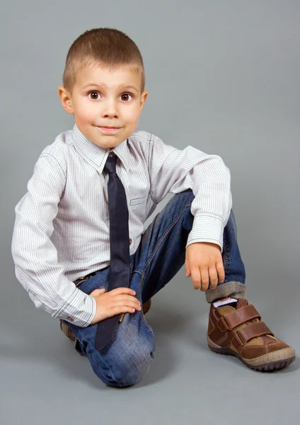 Il ragazzo siede su uno sfondo grigio Fotografia Stock