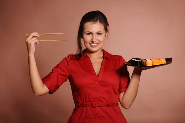 Femme en robe rouge avec baguettes et assiette de sushi — Photo