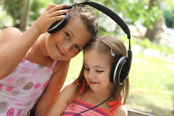Two sisters listen to the music outdoor — Stock Photo, Image