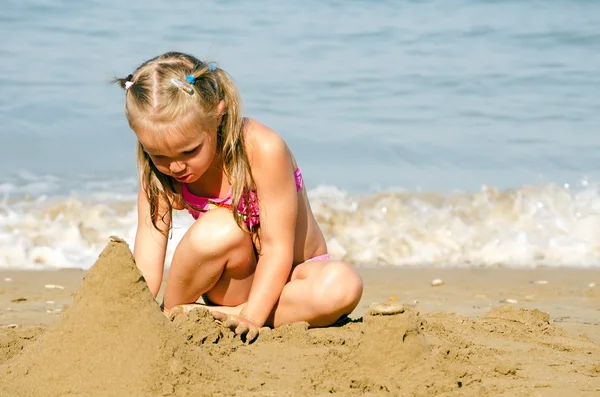 The little girl plays with sand sea coast — Stock Photo, Image