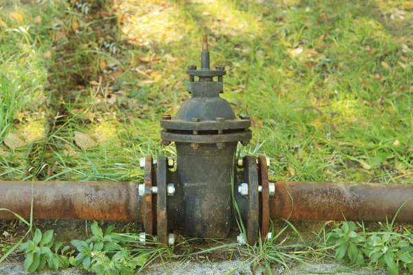 stock image Old rusty pipe with shut-off valve over green grass