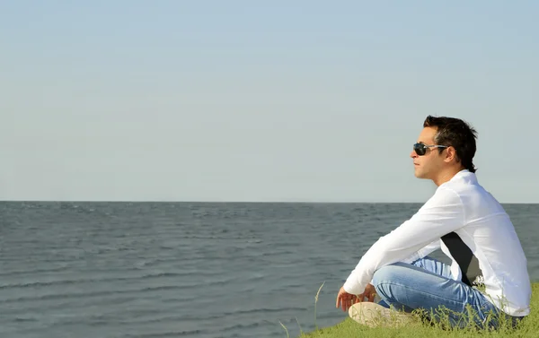 Junger kaukasischer Mann sitzt allein und blickt aufs Meer — Stockfoto