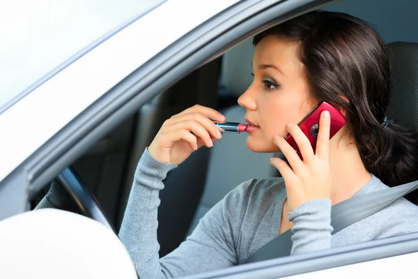 Female driver talking by mobile telephone and doing make-up. — Stock Photo, Image