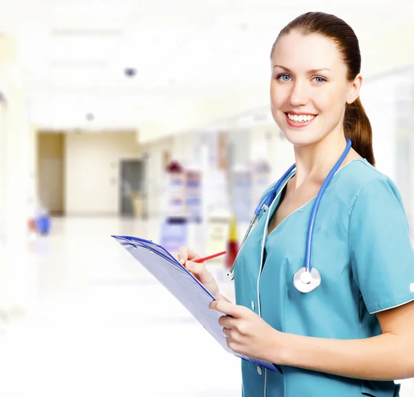 Χαμογελώντας ιατρός με πρόχειρο σε ένα διάδρομο με ένα νοσοκομείο — Φωτογραφία Αρχείου