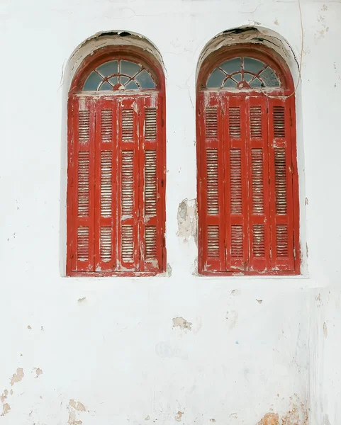 Twee rode ramen met houten luiken op de oude gebarsten witgekalkte muur. b — Stockfoto