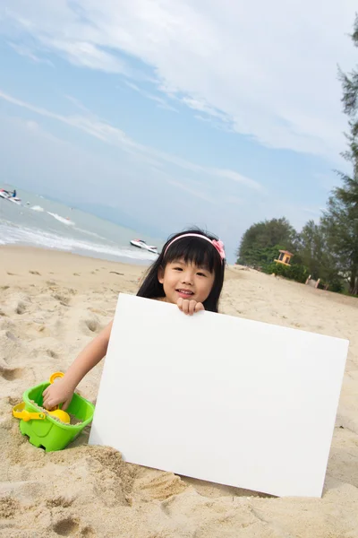Kleines Mädchen hält ein weißes Brett am Strand — Stockfoto
