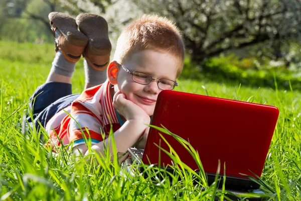 Хлопчик використовує свій ноутбук на відкритому повітрі в парку на траві — стокове фото